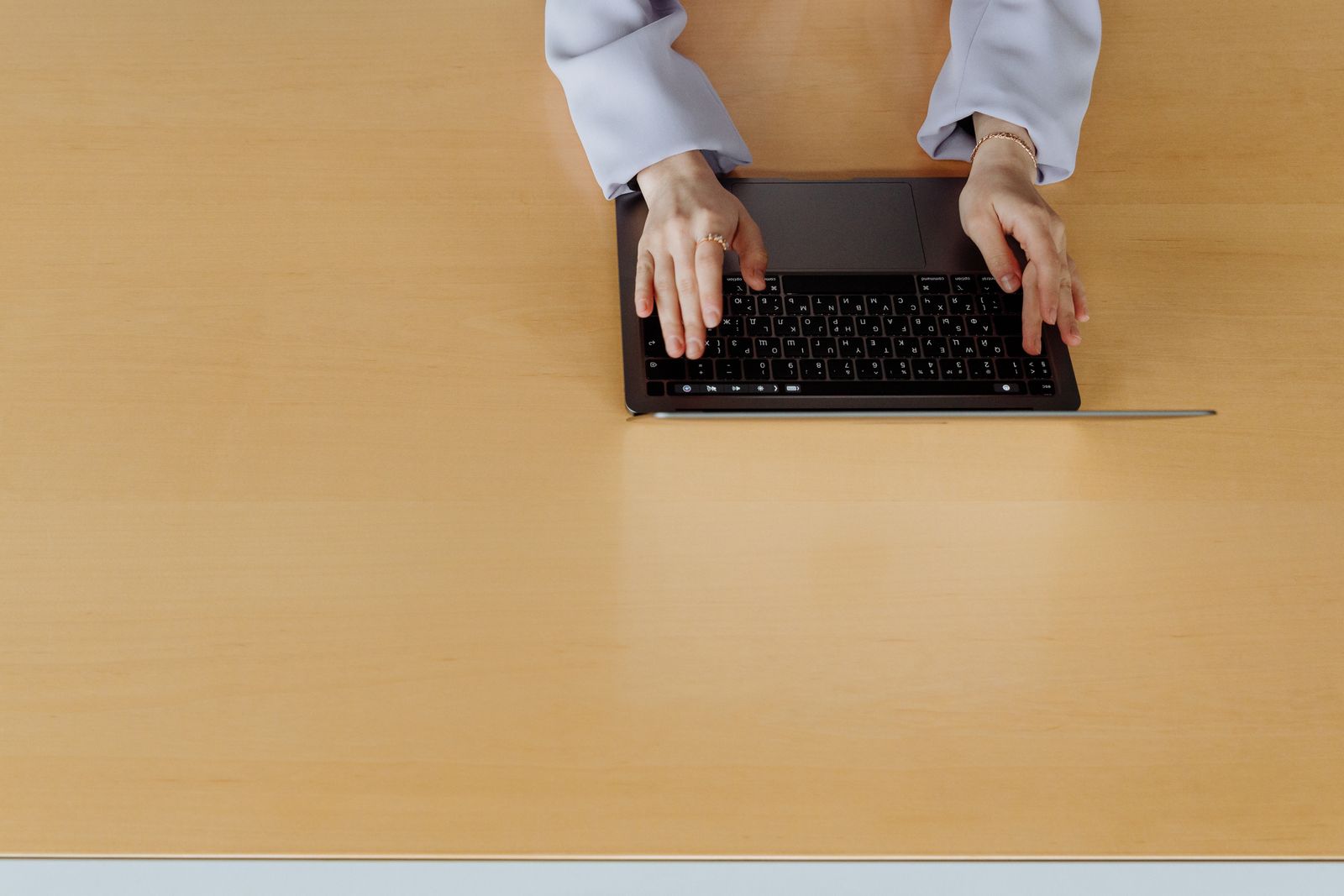 Overhead view of hands typing on a laptop at an otherwise clear wooden desk