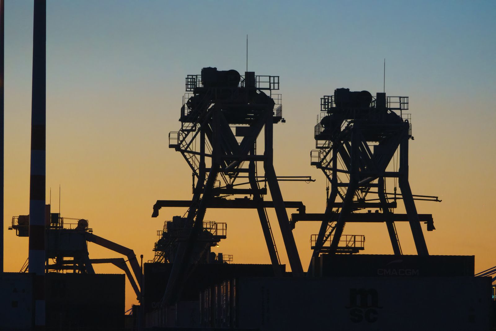 Container cranes silhouetted against a warm dusk sky at a working port