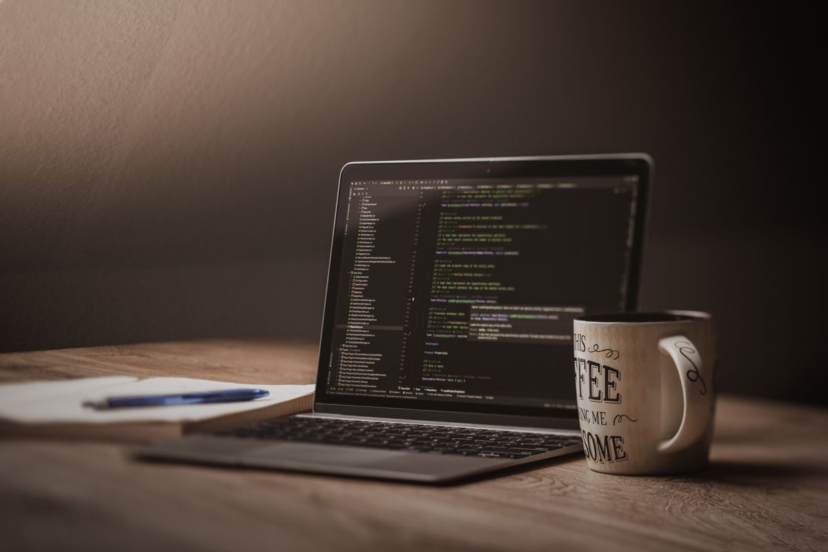 Laptop screen glowing over a warm dim desk with a notebook, pen and coffee mug