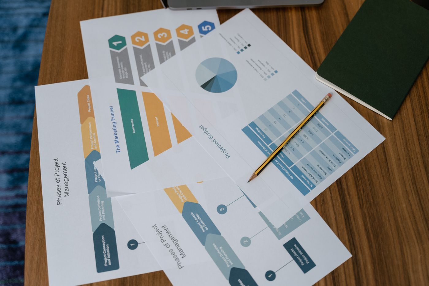 Printed process maps and charts spread across a warm wooden table, a pencil resting mid-markup