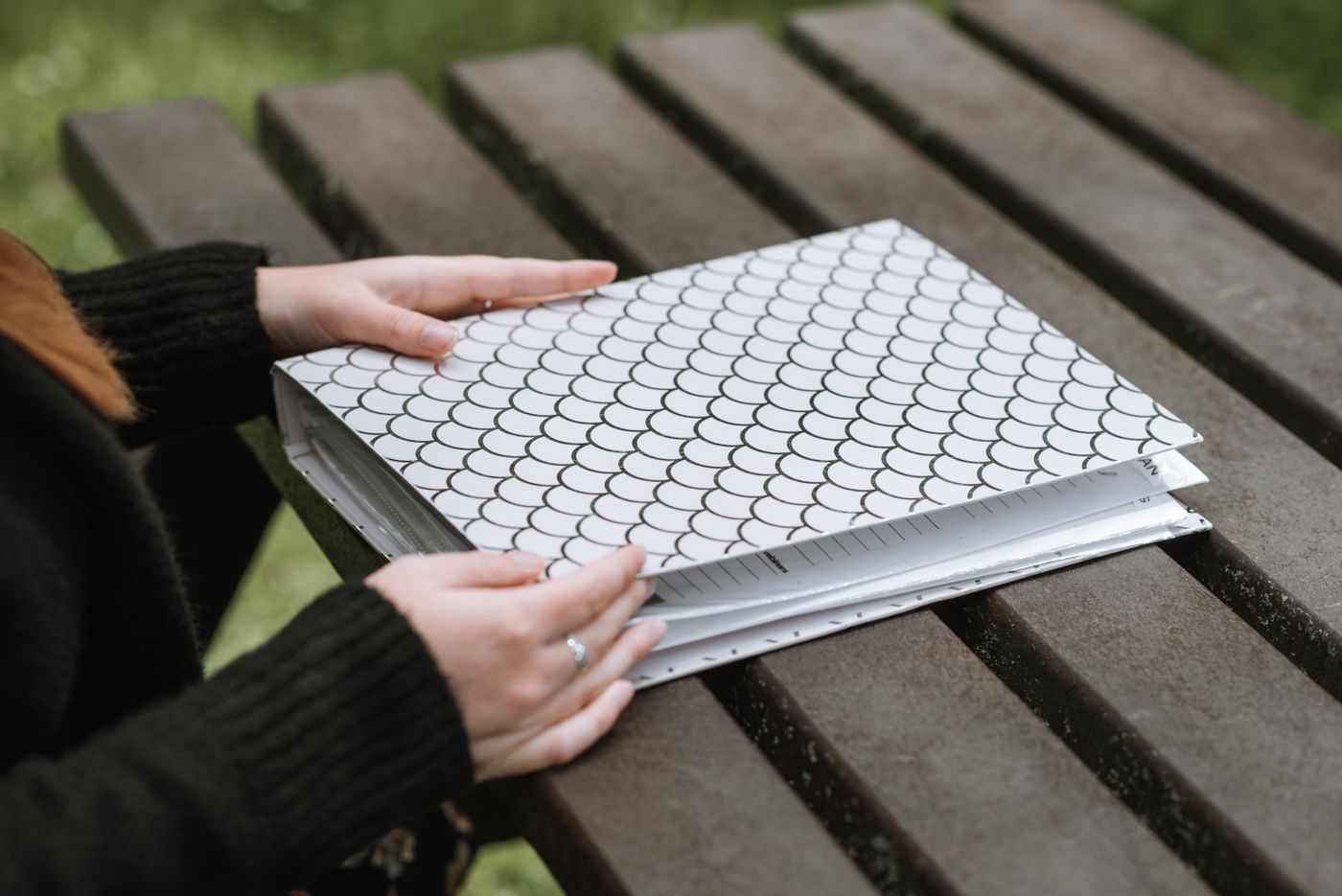 Two hands opening a bound, tabbed playbook on a dark wooden table, faces out of frame